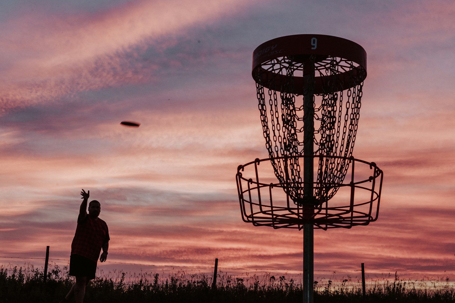 A silhouette of a man throwing a frisbee at a frisbee golf